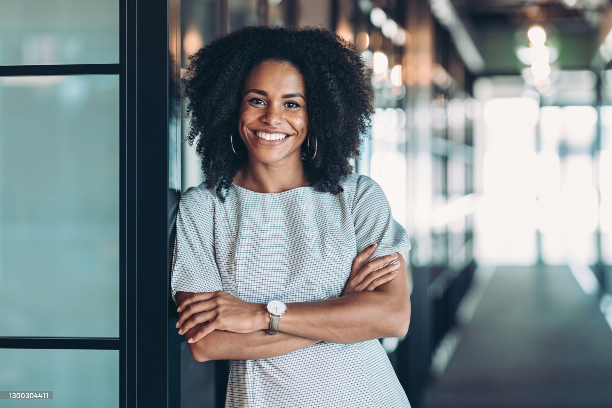 Jonge vrouw kijkt lachend in de camera met haar armen over elkaar