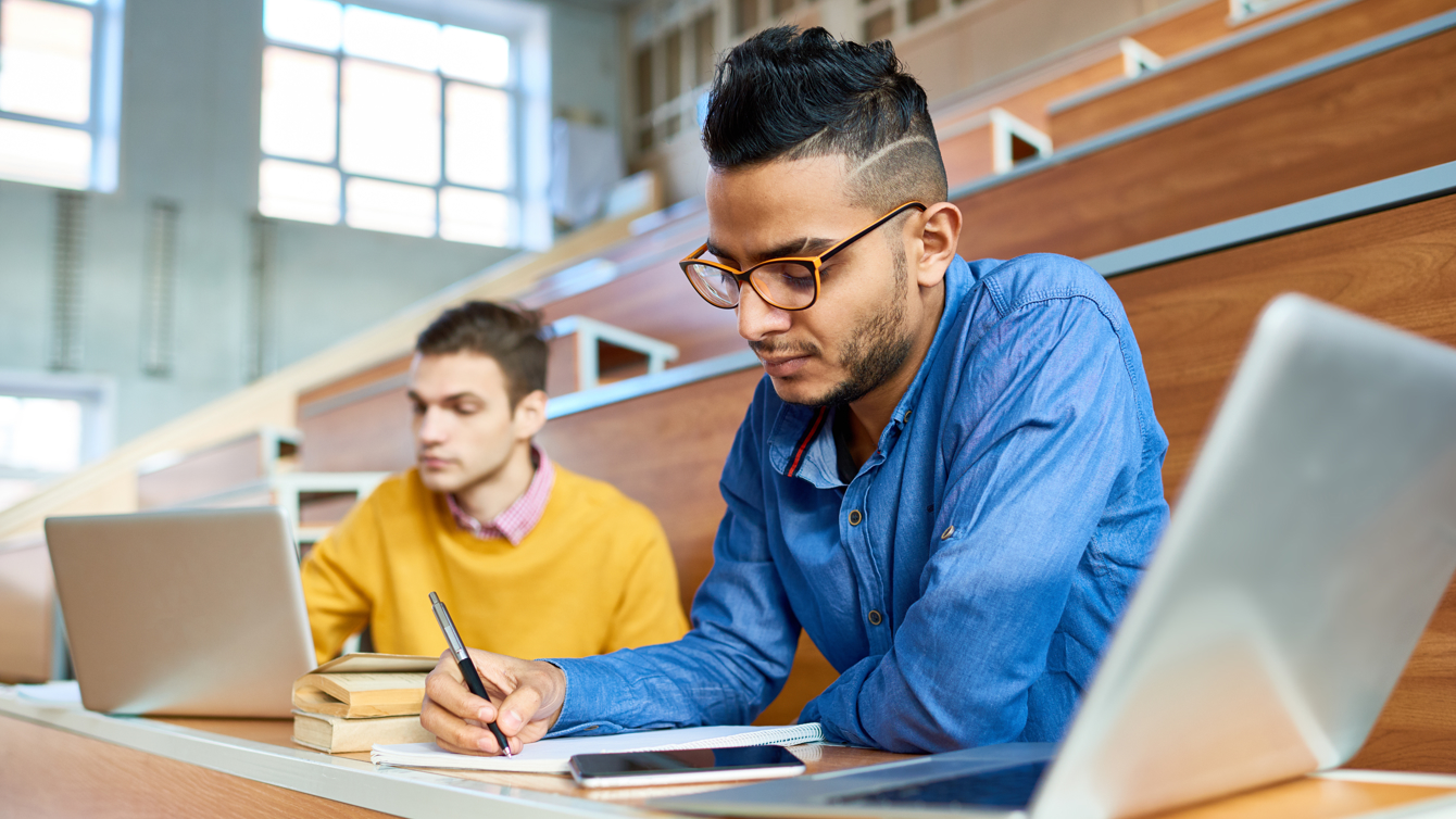 Studenten in een lege collegezaal met laptop en notitieboekje aan het werk