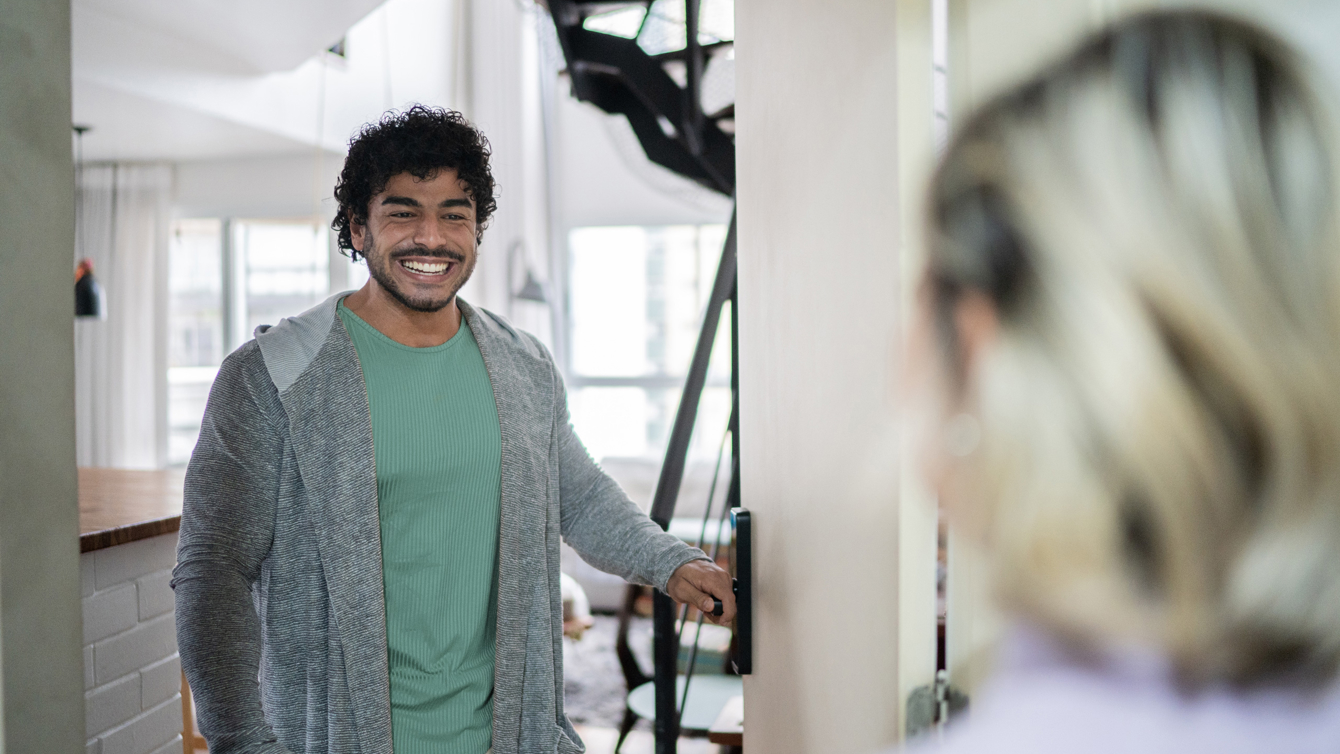 Lachende man doet de voordeur open voor iemand die aan de deur staat