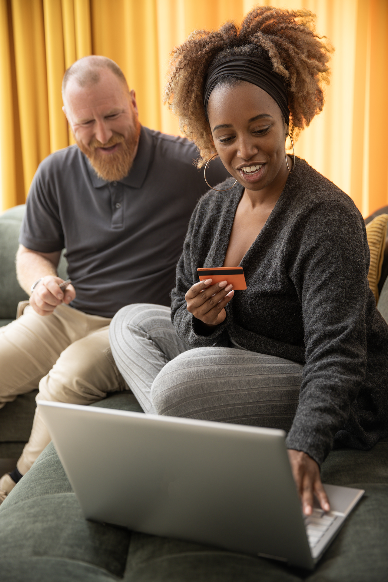 Man en vrouw achter de laptop op de bank met een bankpas in de hand