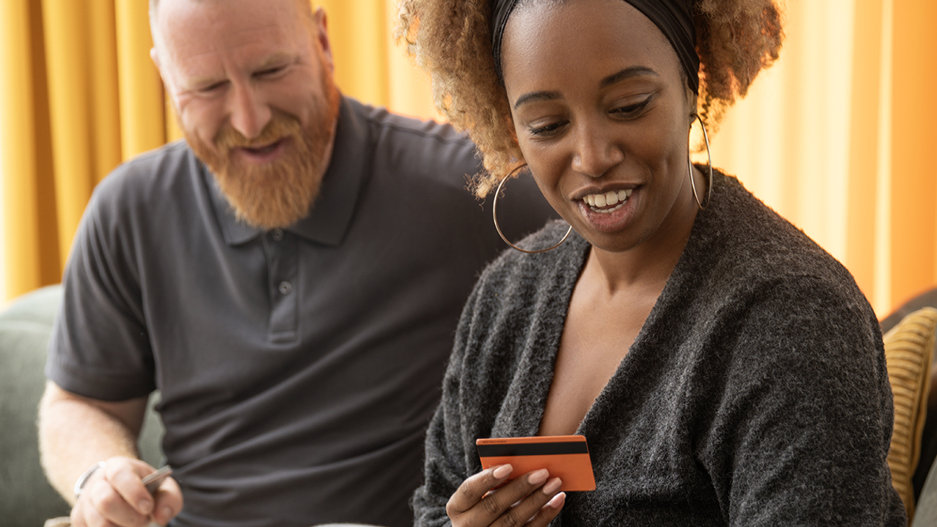 Man en vrouw achter de laptop op de bank met een bankpas in de hand